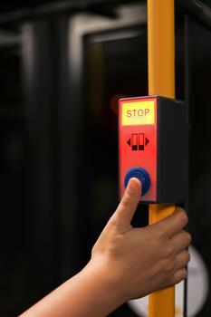 A young girl presses the stop button on a city bus. The button is illuminated in red with the word 'STOP' clearly visible. The bus interior is dark and modern. photo