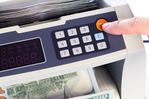 Money counting machine in use with a hand pressing the start button photo