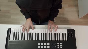 topp se av musikers händer spelar svart och vit midi tangentbord synthesizer med kontrollera panel knappar och knoppar på vit skrivbord, skapande musik i Hem studio uppstart. video