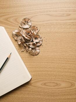 A sharp pencil and shavings on a blank notebook. Vertical creative flat lay on a wooden desk with copy space for text photo