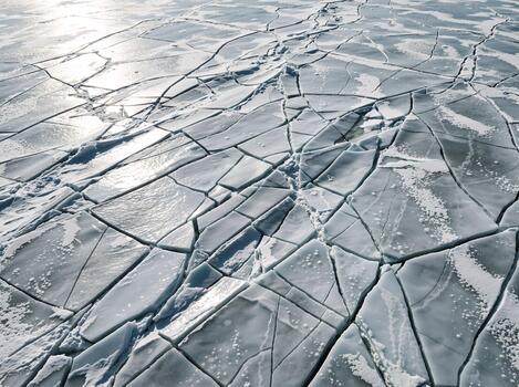 An overhead view of a cracked frozen ice surface. Abstract natural pattern of broken ice in winter. Climate change and global warming background photo