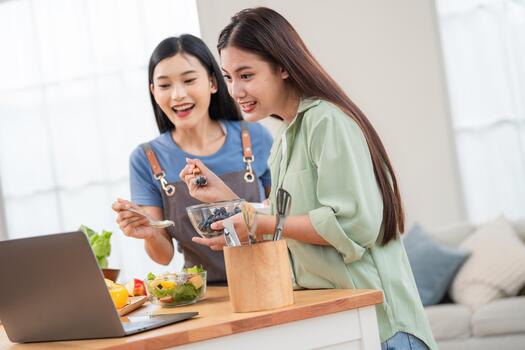 Two friends cook together in a modern kitchen while watching a tutorial during the day photo