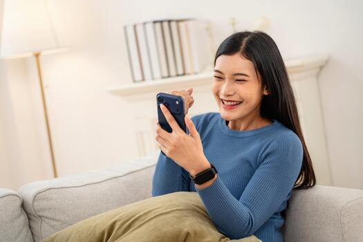 Woman smiles while using her phone on a couch in a cozy room during daytime with soft lighting photo