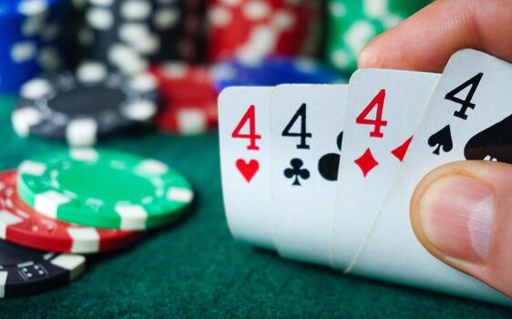 A player holds four cards showing the number four while seated at a poker table. Colorful poker chips are scattered around them, creating a lively gaming atmosphere photo