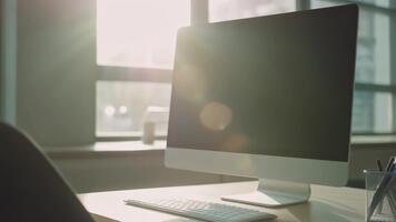 modern kontor skrivbord med ett tömma skrivbordet dator och tangentbord, badade i ljus morgon- solljus. lins bloss på skärm skapa en produktiv arbetsyta. video