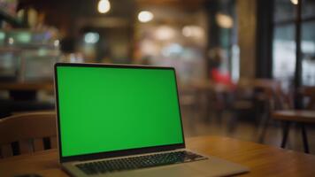 Green Screen Laptop Computer Displayed on a Wooden Table in a Cozy Cafe Setting with Soft Bokeh Lights in the Background Ideal for Creative Edits and Mockups video