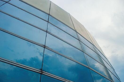 Exterior view of a modern office building with blue glass windows reflecting the sky and clouds, showcasing contemporary architecture and urban development under overcast sky. photo