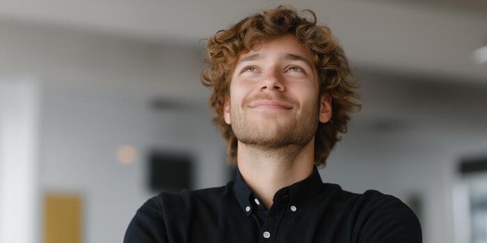 sonriente joven hombre mirando arriba con un pensativo expresión mientras en pie adentro en un moderno oficina espacio. foto