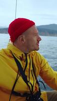 en glad sjöman åtnjuter de lugn av de hav medan bär en ljus gul jacka och en röd mössa, fångad på en avkopplande sjöfart äventyr. video