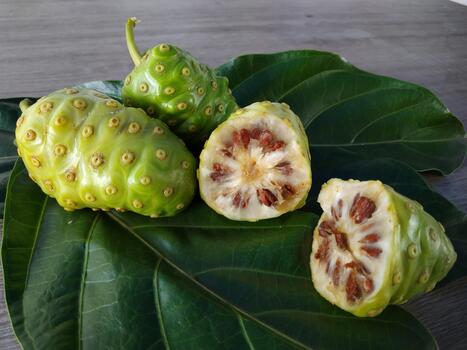Fresh noni fruits displayed on green leaves, showing whole and sliced pieces with visible seeds and natural textures in a rustic setting. photo