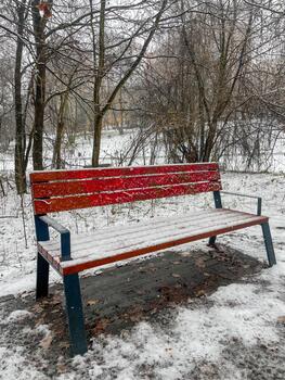 Snow covered park bench in a quiet winter landscape with bare trees and soft snowfall creating a calm seasonal outdoor scene. photo