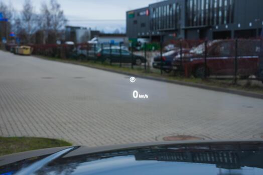A luxury car HUD projects 0 kmh on a head up display and a speed limit icon on the windshield while idling by service bays and parked cars at a modern complex. photo