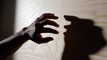 en fängslande samspel av ljus och skugga, skapande en dynamisk dansa mellan en hand och dess silhuett på en trä- yta, full av rörelse video