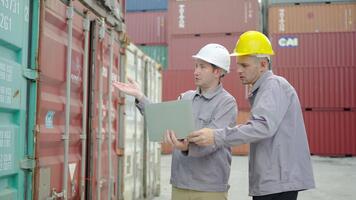 två professionell caucasian ingenjörer klädd i säkerhet uniformer recension logistik operationer på en bärbar dator dator på en behållare terminal. de diskutera strategier för förbättra arbetsflöde och säkerhet video