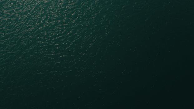 A serene overhead view of a deep teal water surface, its subtle ripples creating a natural, textured pattern background photo