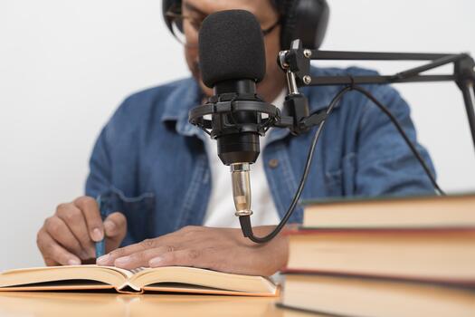 Man recording audio with microphone while reading book at desk for podcast education and learning content photo
