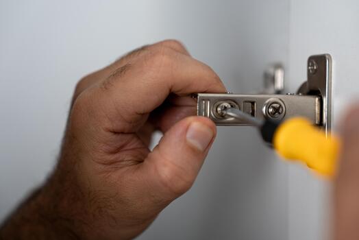 Close-up of hands adjusting a cabinet hinge using a screwdriver. Great for carpentry, DIY content, furniture setup and hardware-related projects. photo
