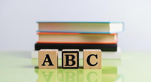 Wooden alphabet blocks displaying ABC on a reflective green surface with stacked books in the background symbolizing early childhood education and a playful learning environment photo