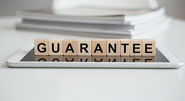 Wooden blocks spelling GUARANTEE resting on a tablet device in a bright clean office environment symbolizing trust reliability and assurance in business and customer service photo