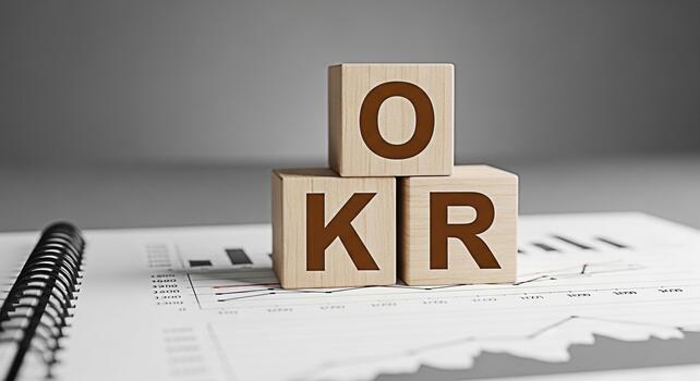 Wooden blocks displaying OKR on a financial report in a corporate office setting representing Objectives and Key Results a popular strategic framework for goal setting and performance tracking photo