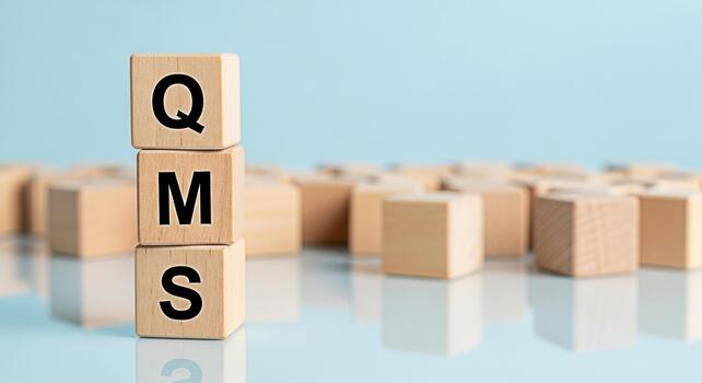 Wooden blocks displaying QMS on a reflective surface representing quality management systems in a business setting conveying a sense of order control and adherence to standards for operational excelle photo