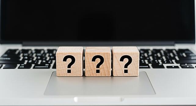 Three wooden blocks displaying question marks resting on a laptop keyboard in a bright office symbolizing uncertainty problemsolving and the need for answers in the digital age photo