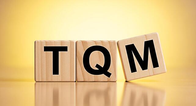 Wooden blocks spelling TQM on a reflective surface against a golden background representing Total Quality Management and a commitment to excellence in business and manufacturing processes photo