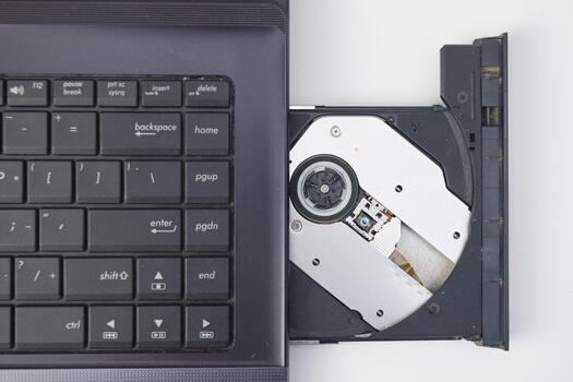 Top view of laptop keyboard with open CD drive showing optical disc mechanism, minimal tech photo suitable for repair, hardware, or data transfer concept.