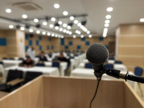 A microphone on a podium and a conference hall waiting in the blurred background. Presentation, speech, and event themes. photo