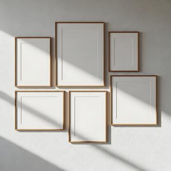A collection of various sized empty picture frames with thin wooden borders arranged artfully on a textured concrete wall with sunlight photo
