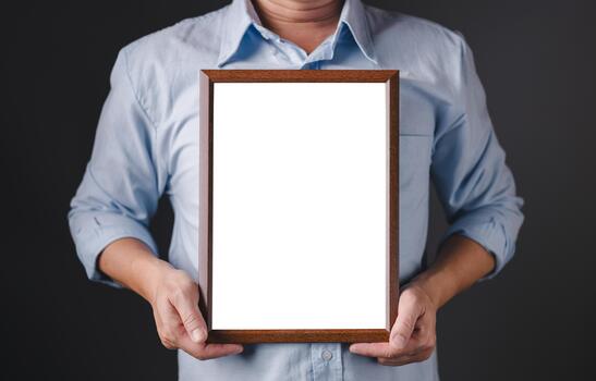 A person in a light blue shirt is holding a vertical wooden frame with a blank white space in the center, offering a clean, empty canvas ideal for text, design, branding, or message display. photo