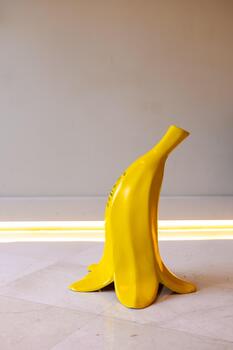 un brillante amarillo plátano escultura soportes vertical en un suave superficie. el antecedentes es minimalista con suave Encendiendo, enfatizando el juguetón diseño foto