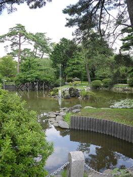 tranquil Japanese garden pond with lily pads, a central fountain, and reflected clouds, bordered by a chain fence. photo