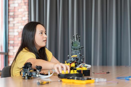 Young Asian Girl Building and Programming Robotic Arm in STEM Class, Student Assembling Robot Components for Science and Technology Project, Close-up of Child's Hand Working on Robot Kit photo
