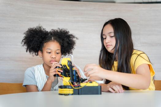 Young Students Controlling a Prototype with Joy, Friends Operating a Small Robotic Arm, Diverse Girls Learning Programming Through Remote Controller Game, Hands-on STEM Education photo