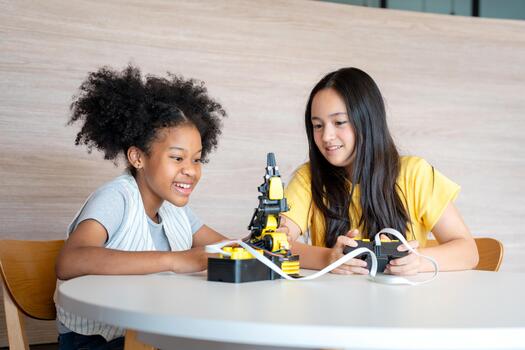 Diverse Girls Learning Programming Through Remote Controller Game, Hands-on STEM Education, Two Young Students Controlling a Prototype with Joy, Friends Operating a Small Robotic Arm photo