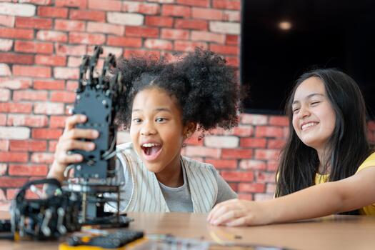 Excited Young Engineers Celebrating Successful Robotics Project in STEM Class, Joyful Children Discovering Technology in Coding Workshop, Girls Inspecting Robotic Arm Prototype photo