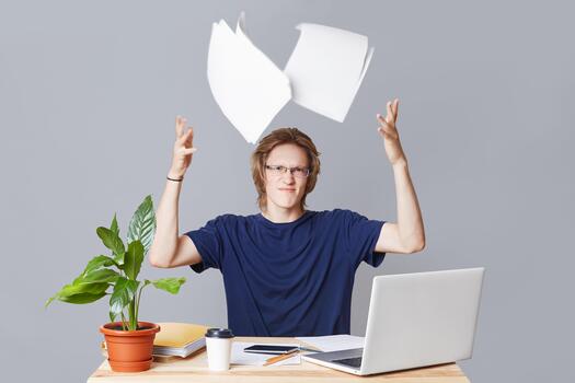 irritado empresario tiene nubes con preparando financiero informe, trabajos a ordenador portátil computadora, lanza documentos con irritación, rodeado con documentos, aislado terminado estudio gris antecedentes foto