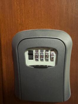 Hand entering code on outdoor key lock box. Close-up of a person inputting a combination code into a secure wall-mounted key lock box near a modern door and light fixture. photo