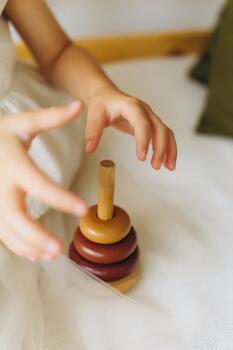 Close-up of a toddlers hands playing with a wooden stacking toy on a soft white bed, natural daylight and warm tones create a cozy, minimalist atmosphere photo