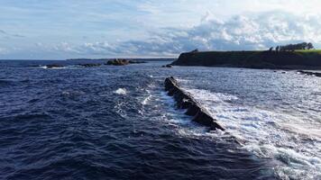 vågor försiktigt knä mot en oländig strandlinje under en omfattande himmel, skapande en lugn kust scen i tidigt eftermiddag ljus på de kant av de hav video