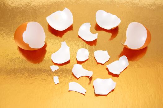 Shattered brown eggs on a glossy golden background, with eggshell pieces spread around, creating a striking and abstract food still life composition photo