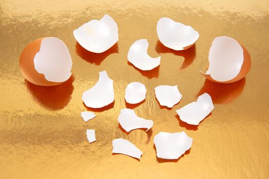A pair of cracked brown eggs with broken shells on a reflective golden surface, casting soft shadows in a warm and artistic food photography setup photo