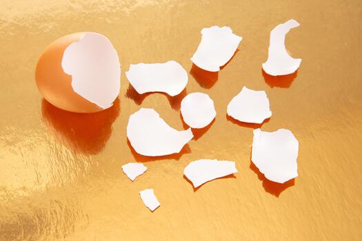 the A pair of cracked brown eggs with broken shells on a reflective golden surface, casting soft shadows in a warm and artistic food photography setup photo