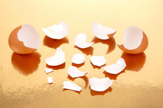 The a Shattered brown eggs on a glossy golden background, with eggshell pieces spread around, creating a striking and abstract food still life composition photo