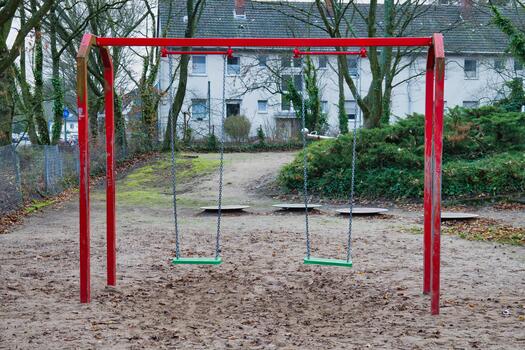vacío rojo marco columpios con verde asientos en arenoso patio de recreo suelo rodeado por arboles y residencial edificios en tranquilo suburbano parque zona foto