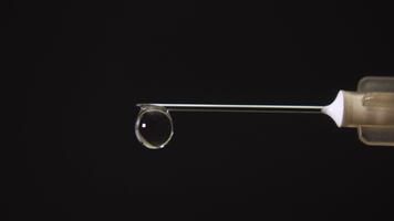 Macro shot of a syringe in low key lighting with a drop of liquid forming at the needle tip, creating a striking medical and cinematic atmosphere. video