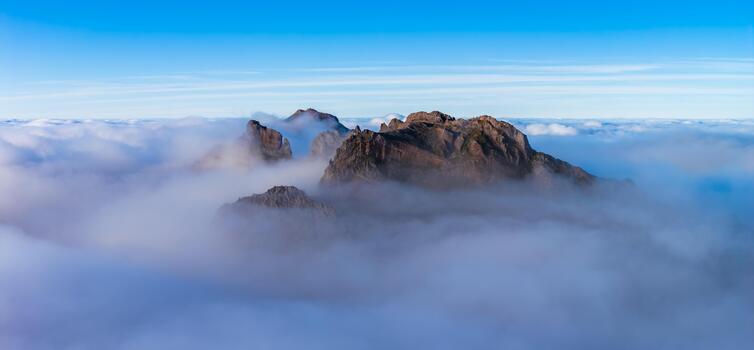 Dark rock spires rise above clouds at Pico do Arieiro in Madeira, Portugal. Wide panoramic view in soft light shows sharp ridgelines and smooth cloud layers. photo