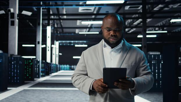 IT professional in server hub ensuring valuable data remains shielded from potential threats using tablet. Worker safeguarding data center against unauthorized access and vulnerabilities, camera A photo