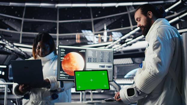 Astronaut monitoring system diagnostics on isolated screen tablet, chatting with colleague during space mission. Teamworking cosmonauts using mockup during cosmic expedition photo